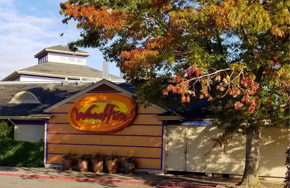 Exterior of Anthony's WoodFire Grill, orange facade, autumn tree.