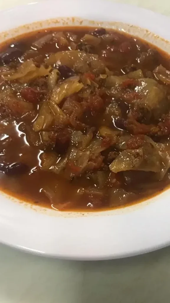 Reddish-brown stew with cabbage, tomatoes, and beans in a white bowl.