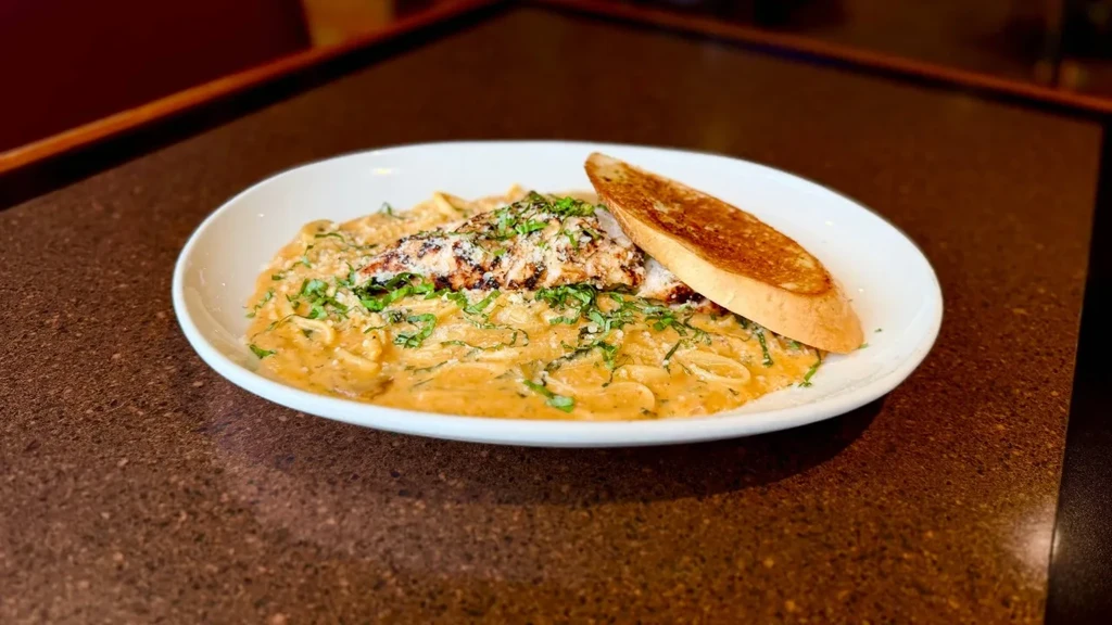 Close-up of creamy pasta, grilled protein, cheese, herbs, and toasted bread.