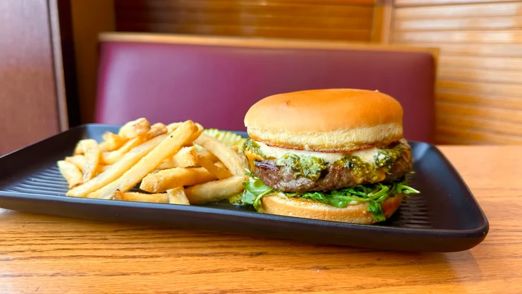 Close-up of burger with melted cheese, pesto, fries, and pickle.