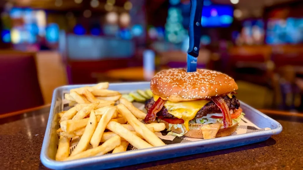 Burger with bacon, cheese, fries, and pickles on a restaurant tray.