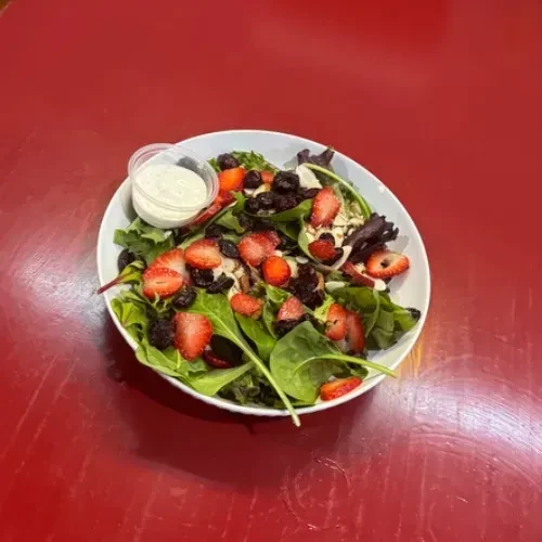 Overhead green salad with strawberries, dark berries, and creamy dressing.