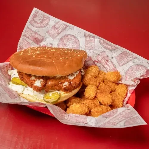 Crispy fried chicken sandwich, pickles, and tater tots in a red basket.