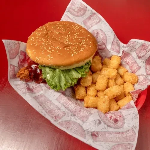 Fried chicken sandwich with lettuce and tater tots in a red basket.