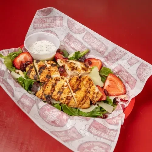 Top-down grilled chicken salad with strawberries, cranberries, cheese, and dressing.