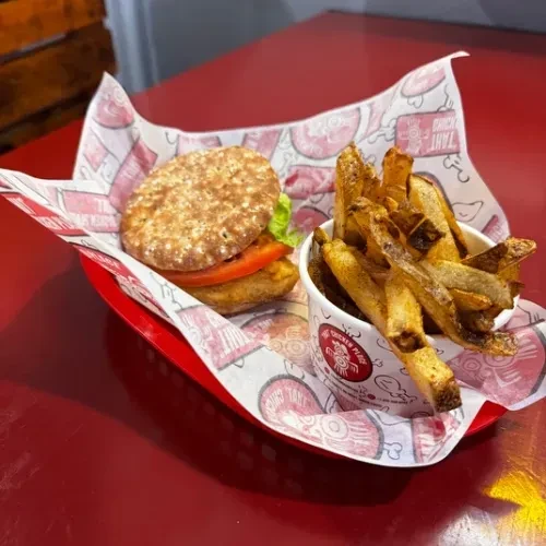 Burger with lettuce, tomato, and skin-on fries on a red table.