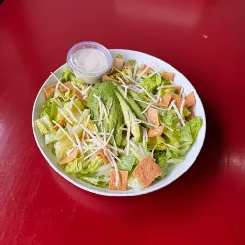 Salad with lettuce, avocado, white strings, crispy pieces, and dressing.