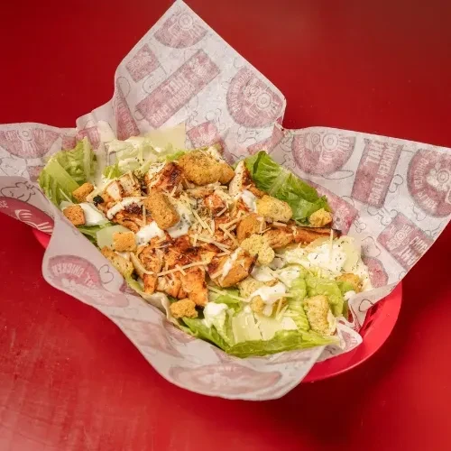 Close-up, top-down Caesar salad with grilled chicken in red basket.