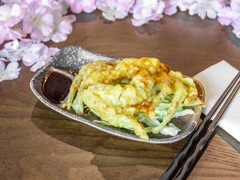 Deep-fried tempura or crab with cabbage, dipping sauce, chopsticks, cherry blossoms.