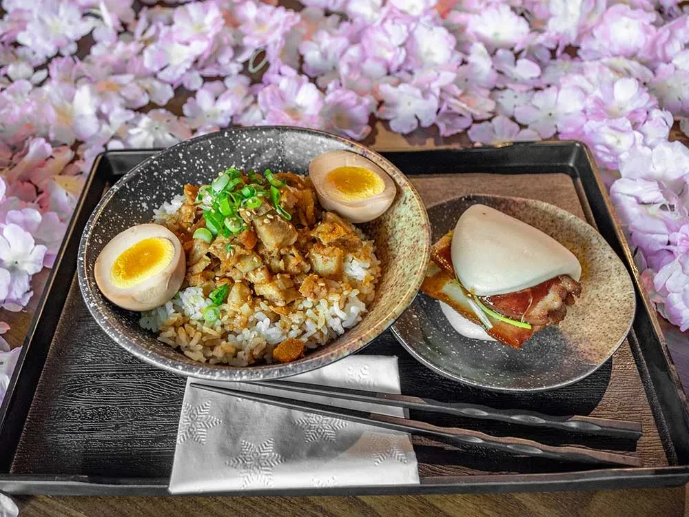 Rice bowl with chopped meat and eggs, bacon bao bun on tray.