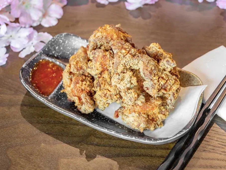 Golden-brown fried chicken, red sauce, chopsticks, and floral background.