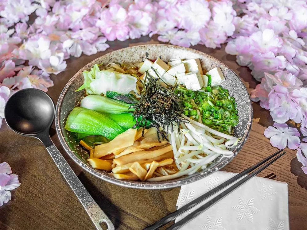 Vibrant tofu noodle soup with bok choy, chopsticks, and cherry blossoms.