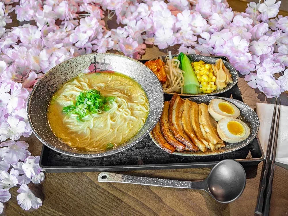 A ramen set with pork, eggs, vegetables, and pink cherry blossoms.