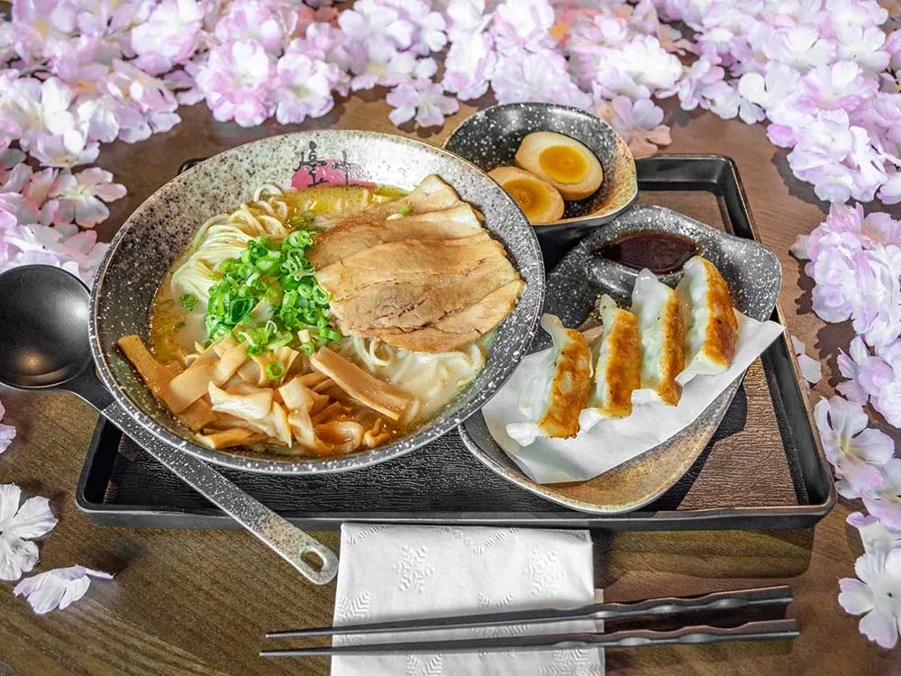 Overhead shot of Japanese ramen, gyoza, and eggs with cherry blossoms.