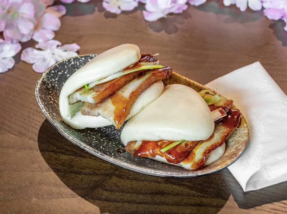 Two steamed pork belly bao buns with scallions on a dark plate.