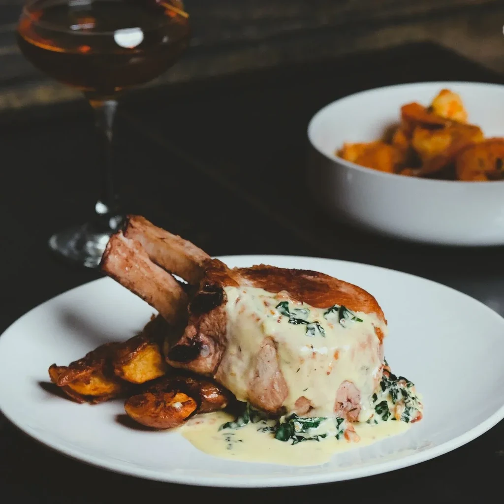 Plated bone-in pork chop with creamy herb sauce and roasted potatoes.
