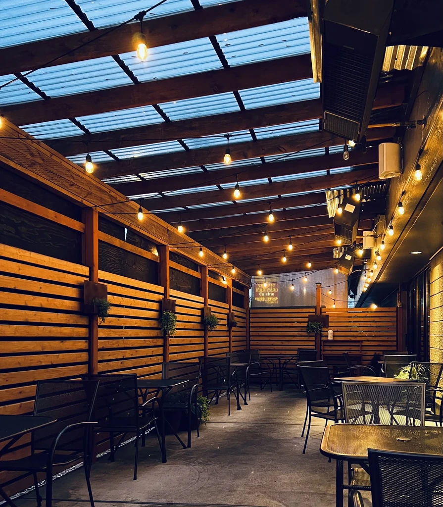 Empty restaurant patio with string lights, wooden walls, and metal tables.