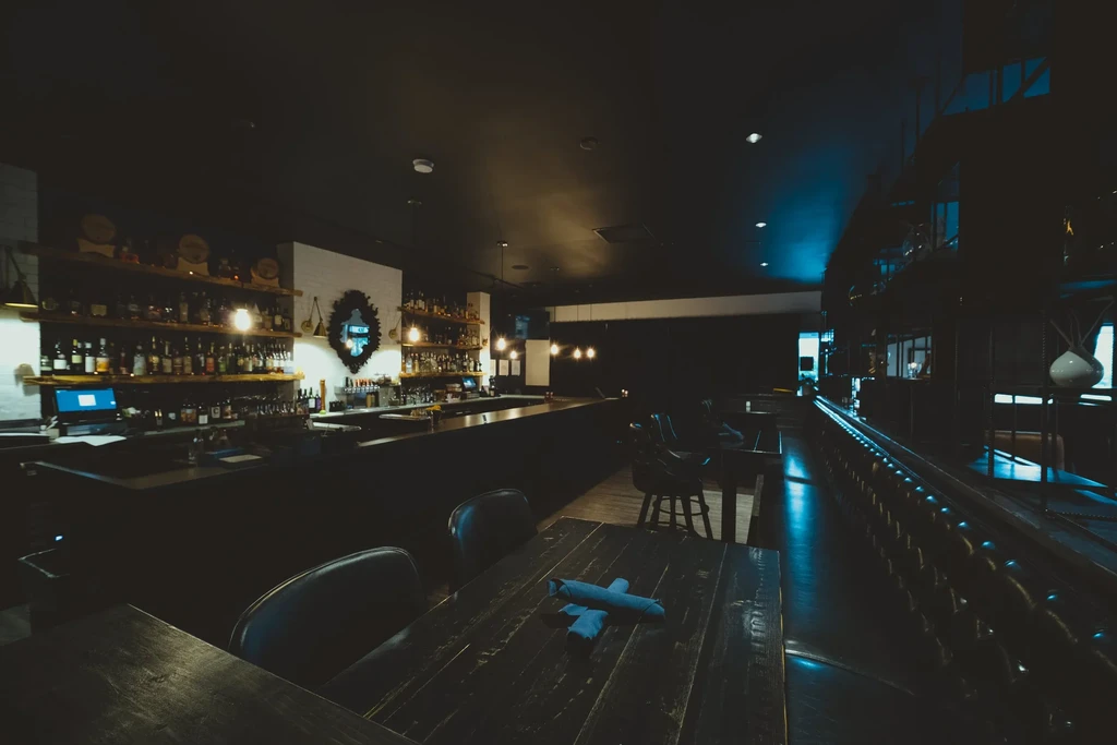 Dark bar interior: stocked counter, warm lights, contrasting electric blue glow.