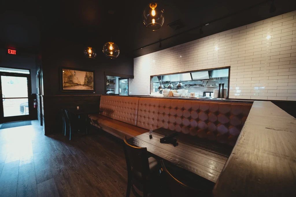 Dark restaurant interior with a brown booth and bright kitchen pass-through.