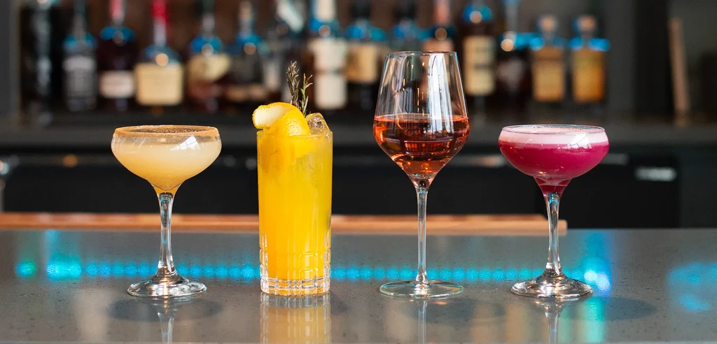 Four colorful drinks in various glasses on a reflective bar.