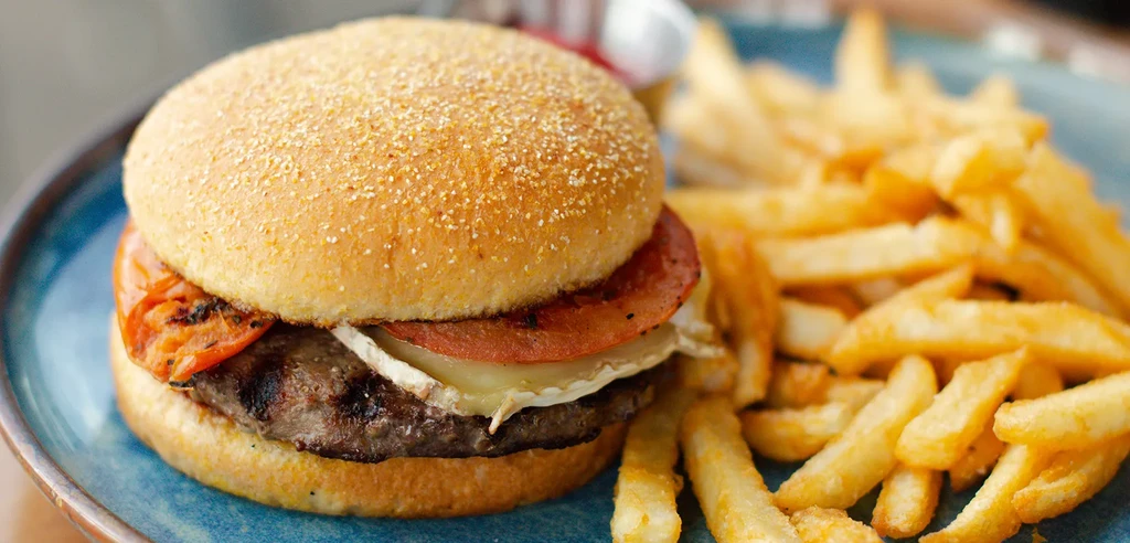Close-up of a burger with cheese and crispy fries on a blue plate.