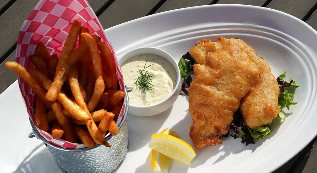 Battered fish, fries in a bucket, tartar sauce, and lemon wedges.