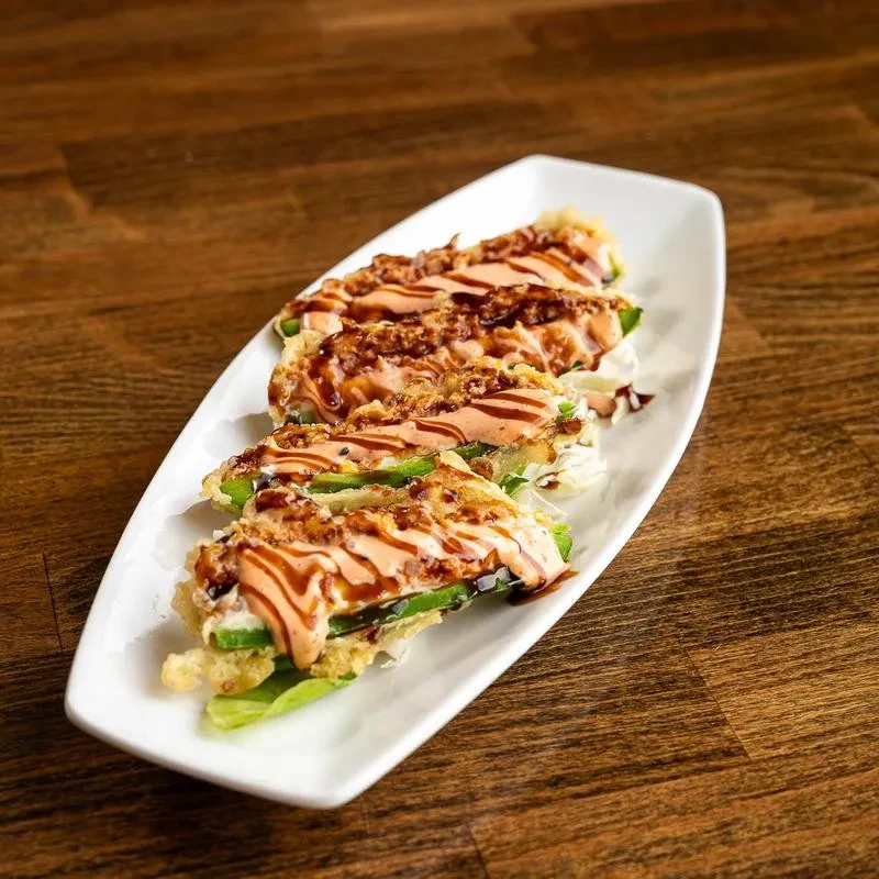 Plate of fried sushi rolls with orange sauce and crunchy toppings.