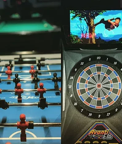 Foosball table, electronic dartboard, and video game screen in a bar.