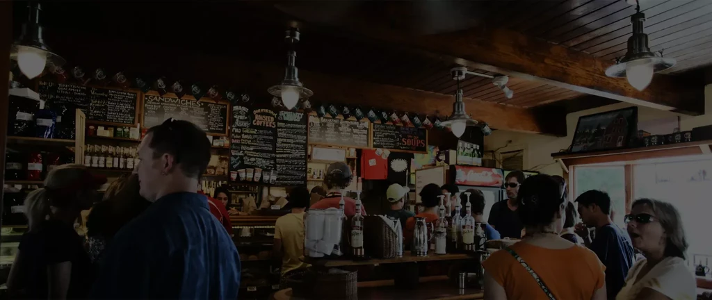 Customers at a rustic, dimly lit cafe counter with menu chalkboards.