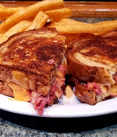 Grilled corned beef or pastrami sandwich with melted cheese and french fries.