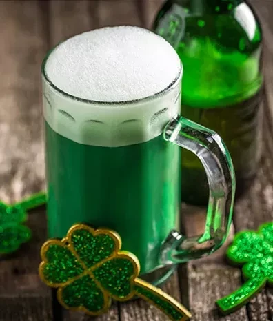 Green beer in a mug with shamrocks on a rustic wooden surface.