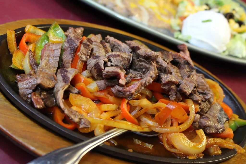 Sizzling beef fajitas with onions and peppers, served on cast iron.