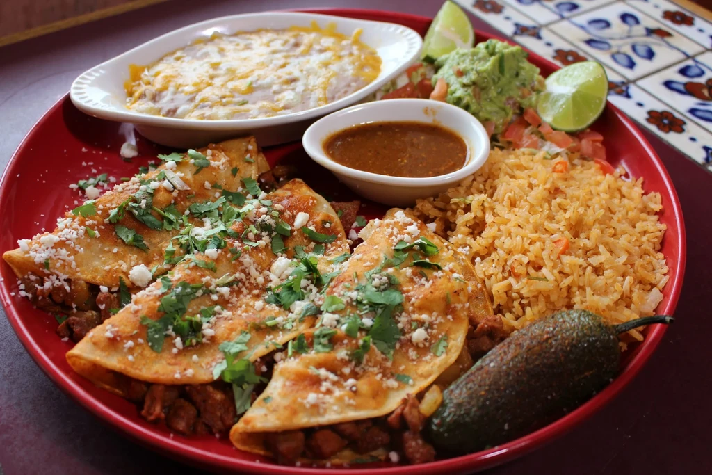 Mexican food platter with enchiladas, rice, beans, guacamole, and lime.