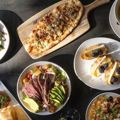 Top-down view of flatbread, steak salad, bruschetta, and other dishes.