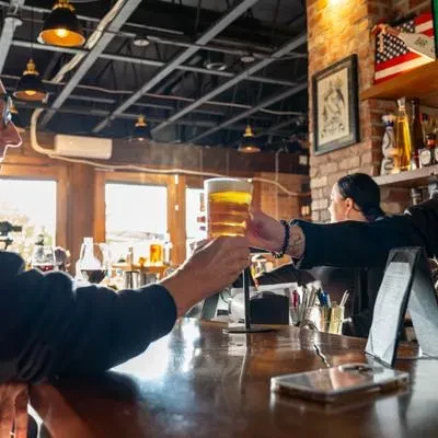 Bartender hands frothy beer to patron over a bar counter.