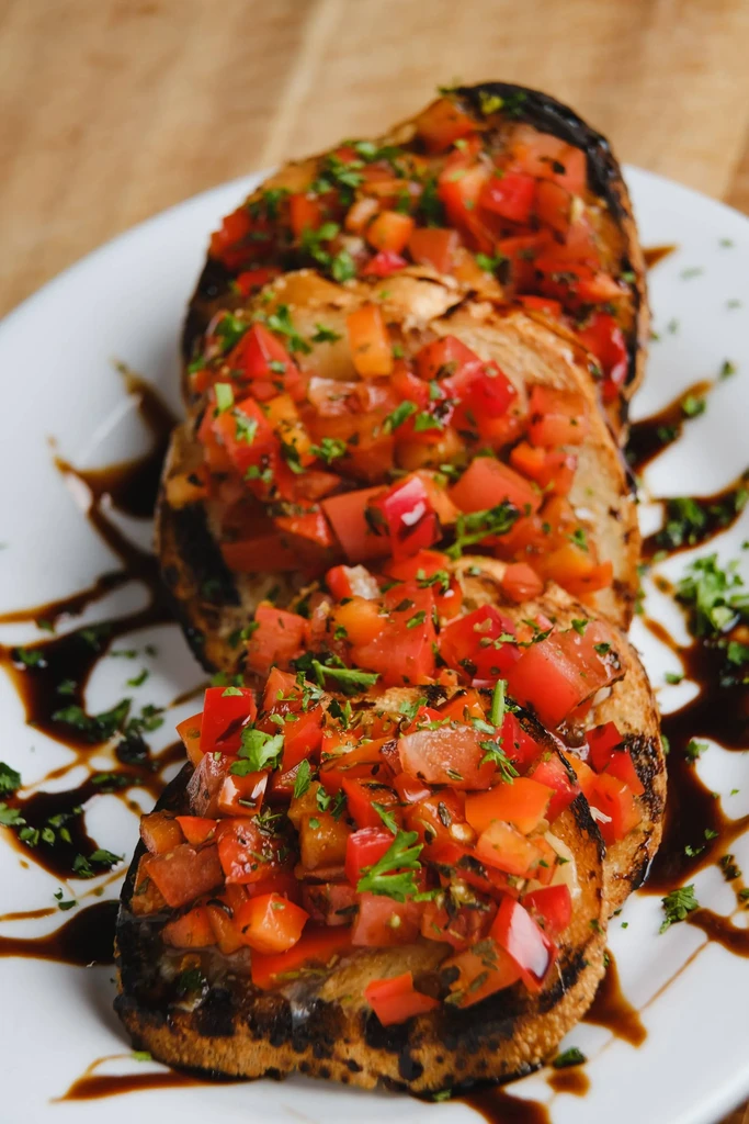 Toasted bruschetta topped with tomatoes, green herbs, and balsamic glaze.
