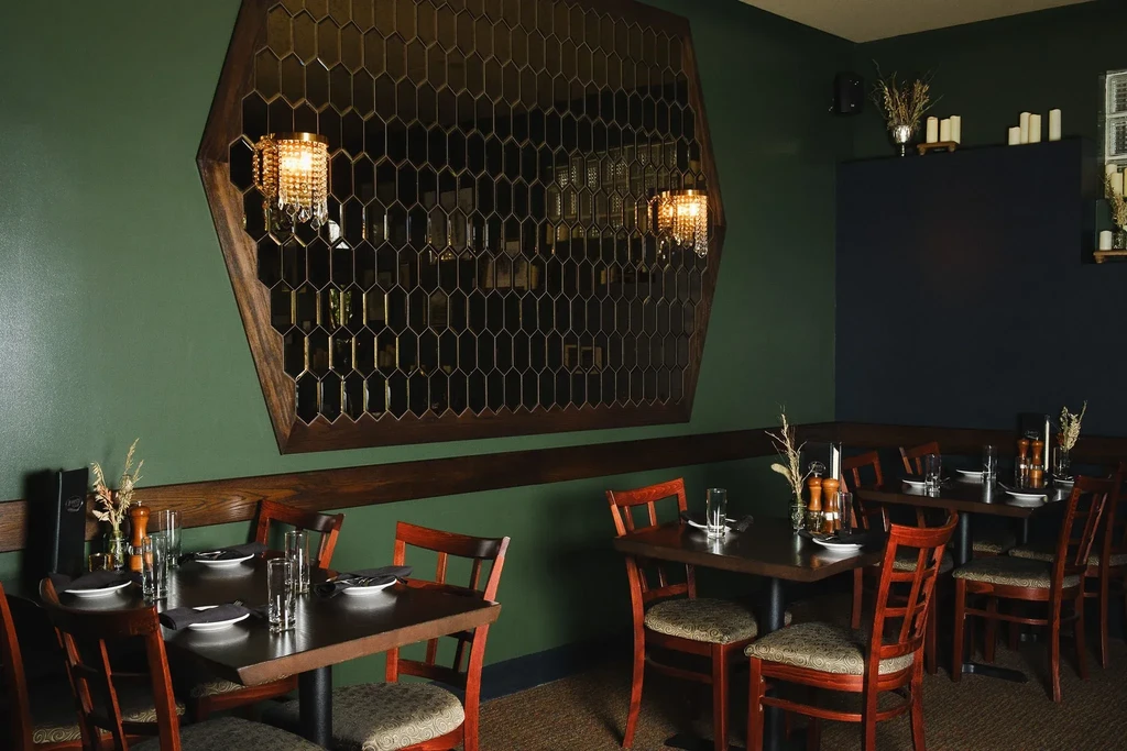 Green-walled restaurant interior featuring a large hexagonal mirror and set tables.