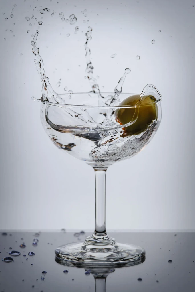 Olive dropping into a coupe cocktail glass, creating a splash.