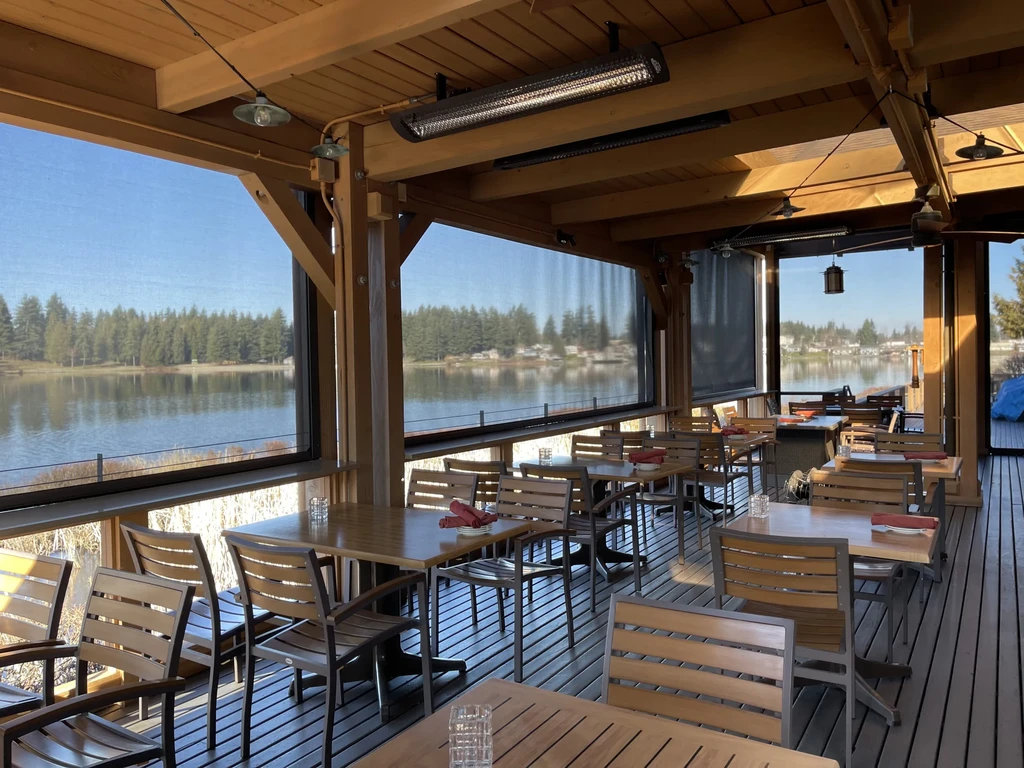 Empty semi-outdoor dining patio overlooks lake and evergreen forest.
