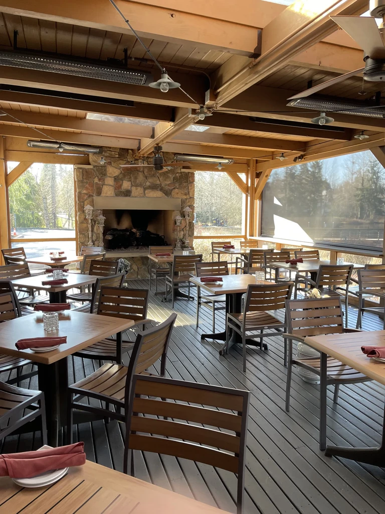 Restaurant patio with dining tables, rustic fireplace, and wood-beamed ceiling.