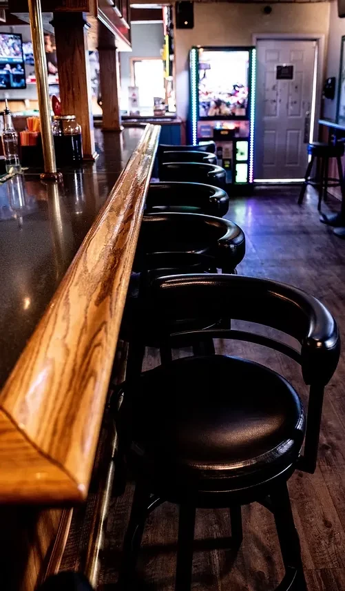 Polished wooden bar counter and five black stools in a dim pub.
