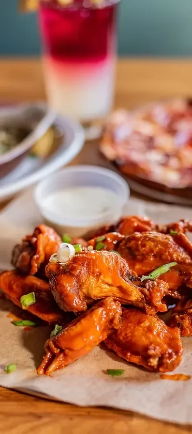 Saucy Buffalo or BBQ chicken wings with green onions and dip.