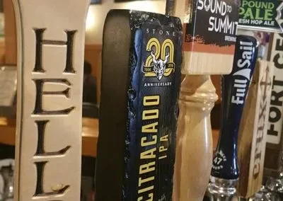 Colorful beer tap handles, including Stone and Full Sail, at a bar.