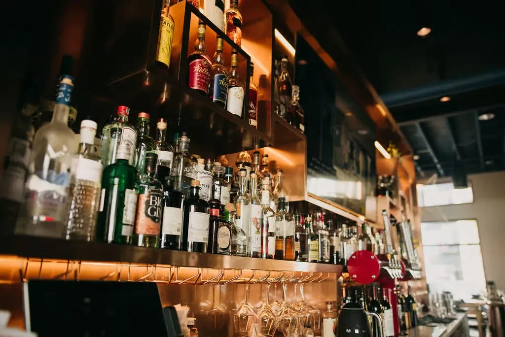 A modern bar features shelves of spirits and inverted hanging glasses.