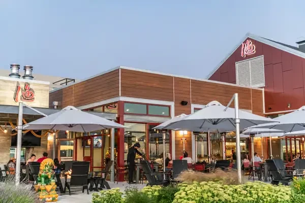 Modern restaurant with red facade, neon logo, and bustling patio dining.
