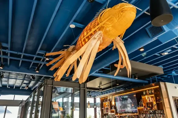 Woven fish sculpture suspended over a modern, brightly lit restaurant bar.