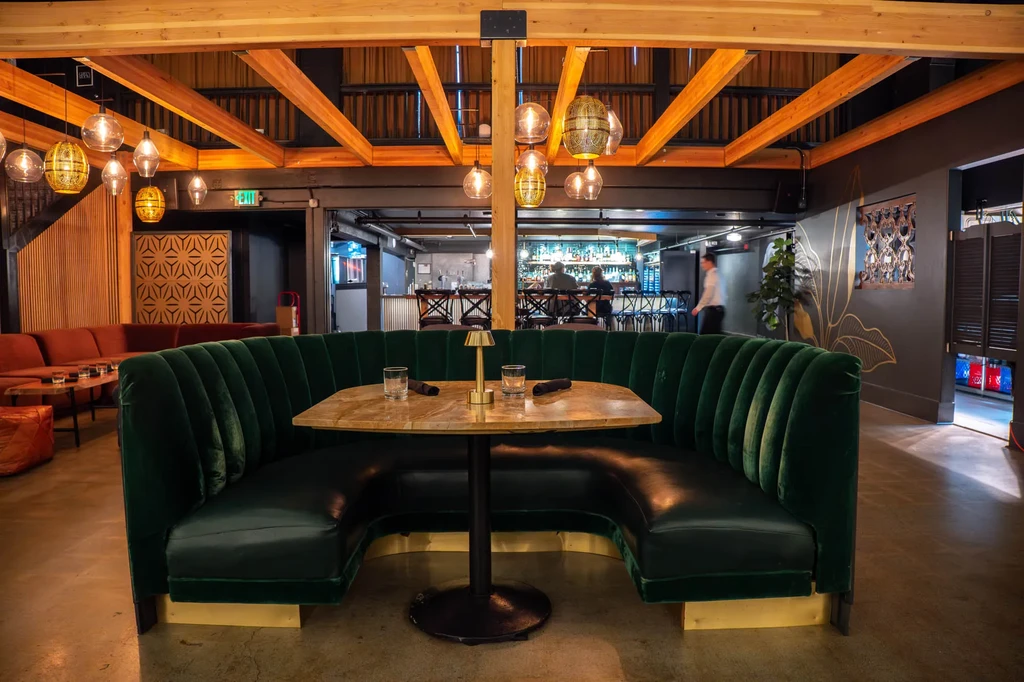Modern restaurant with green velvet booth, wood beams, and warm lighting.