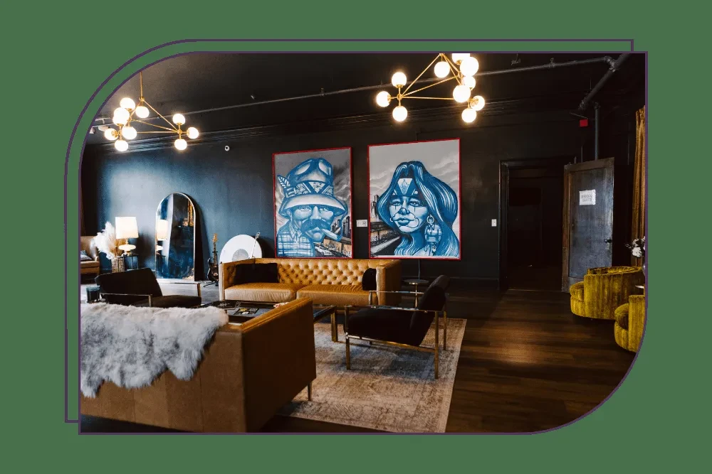 Stylish dark lounge featuring art, camel sofa, and modern chandeliers.