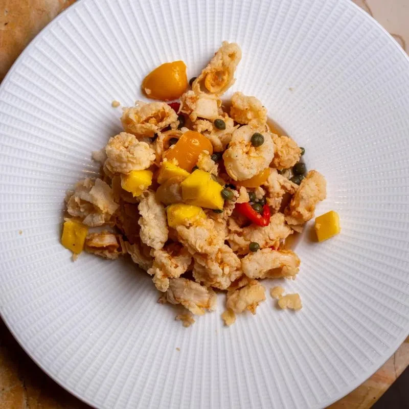 Crispy fried seafood, mango, capers, and chili on a white plate.