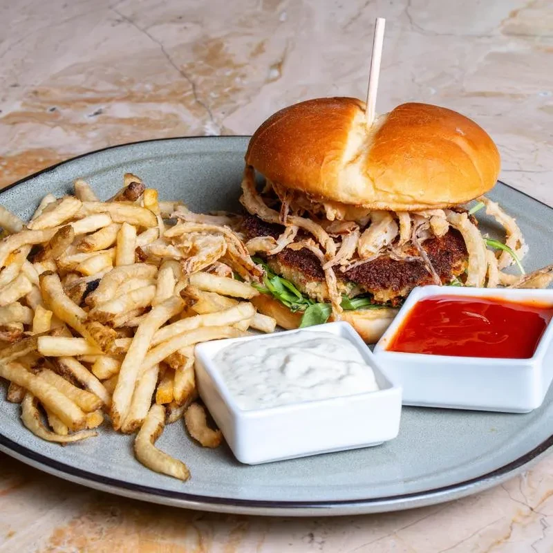 Gourmet burger with crispy onions, fries, ketchup, and creamy white sauce.
